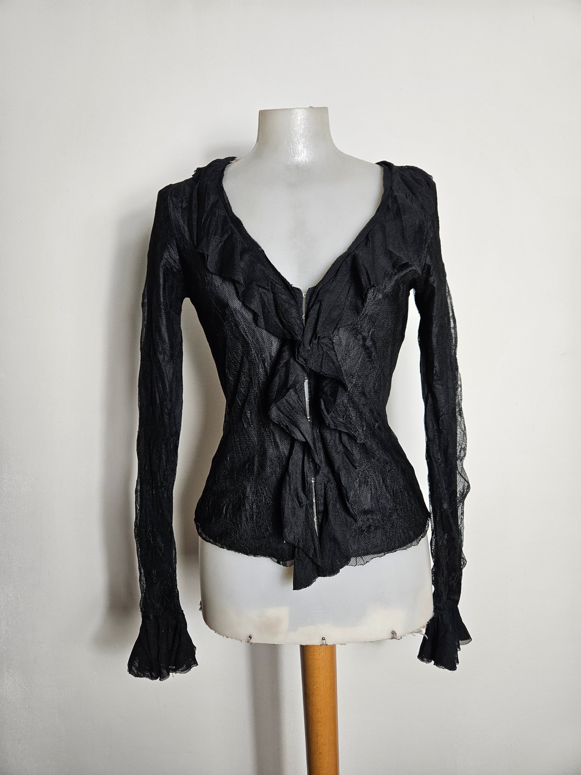 A mystical whimsigoth black long-sleeve top with a sheer textured fabric. Features dramatic ruffled trims along the V-neckline and sleeve cuffs, with a delicate hook-and-eye front closure for a dark fairycore aesthetic.