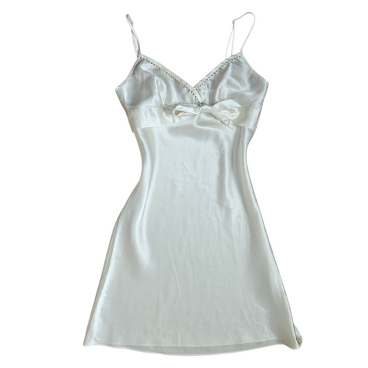 Ivory satin slip dress with delicate straps, V-neckline and underbust bow detail, soft y2k romantic vintage aesthetic.