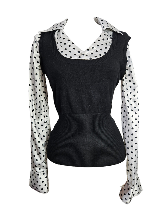 Black sleeveless knit sweater vest layered over a white and black polka dot satin button-down shirt on mannequin. Vintage-inspired 2-in-1 office wear style.