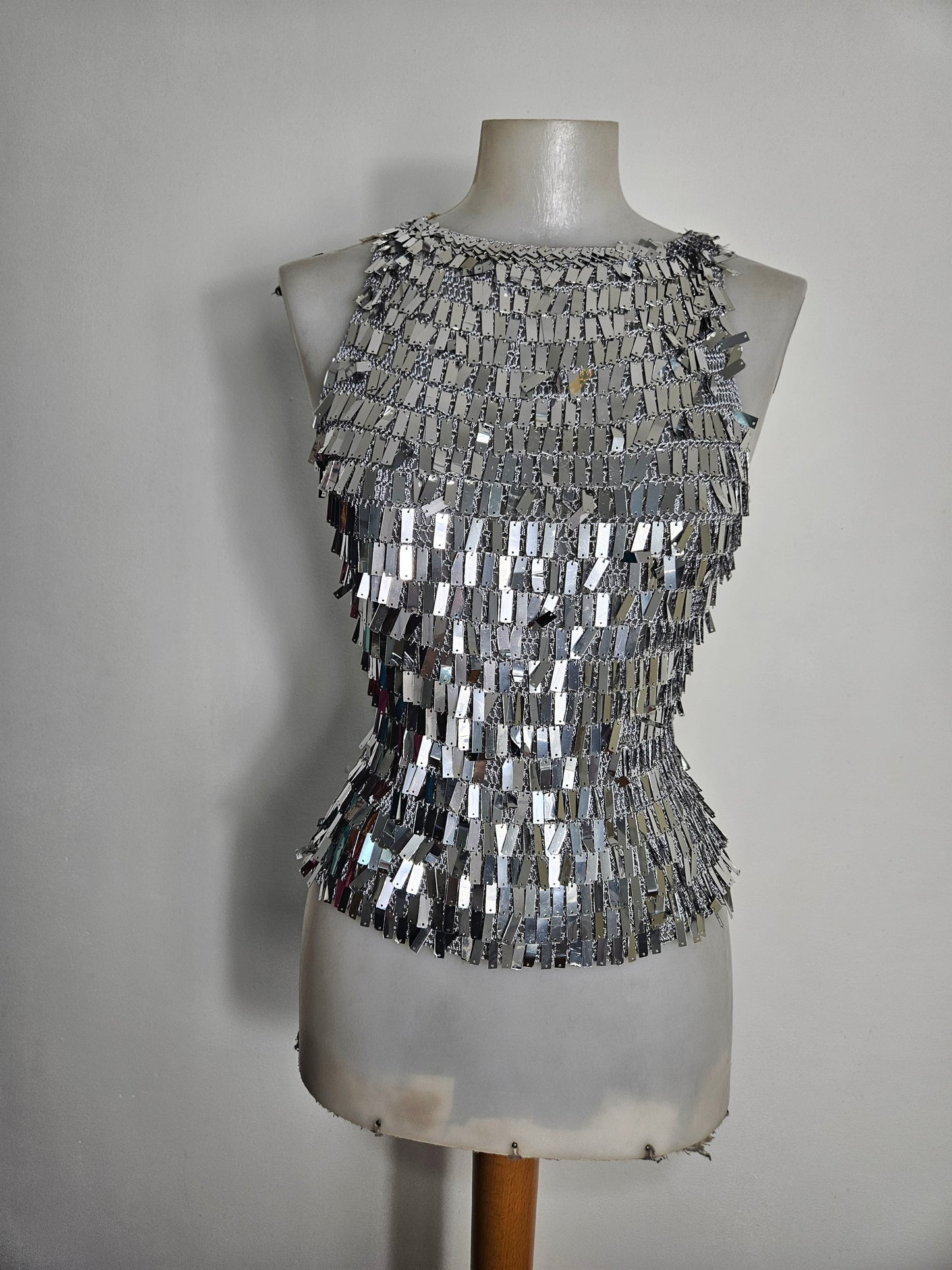 A vintage silver high-neck top on a mannequin with layered, reflective rectangular palettes. Ideal for a Y2K party look or statement festival outfit.