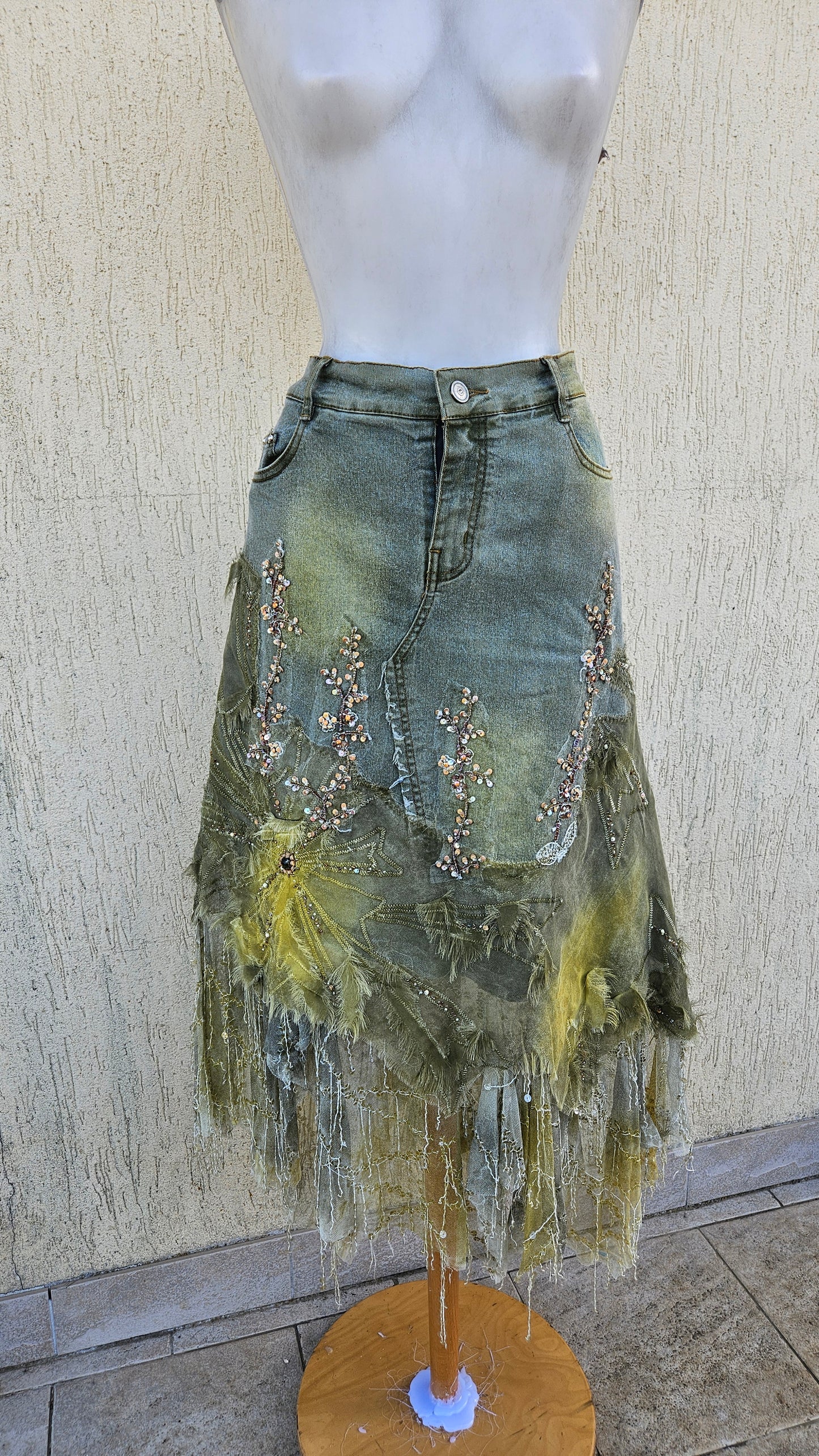 Distressed olive green denim midi skirt with yellow mesh overlays, floral bead embroidery, and shredded fringe hem. Fairy grunge aesthetic on mannequin.