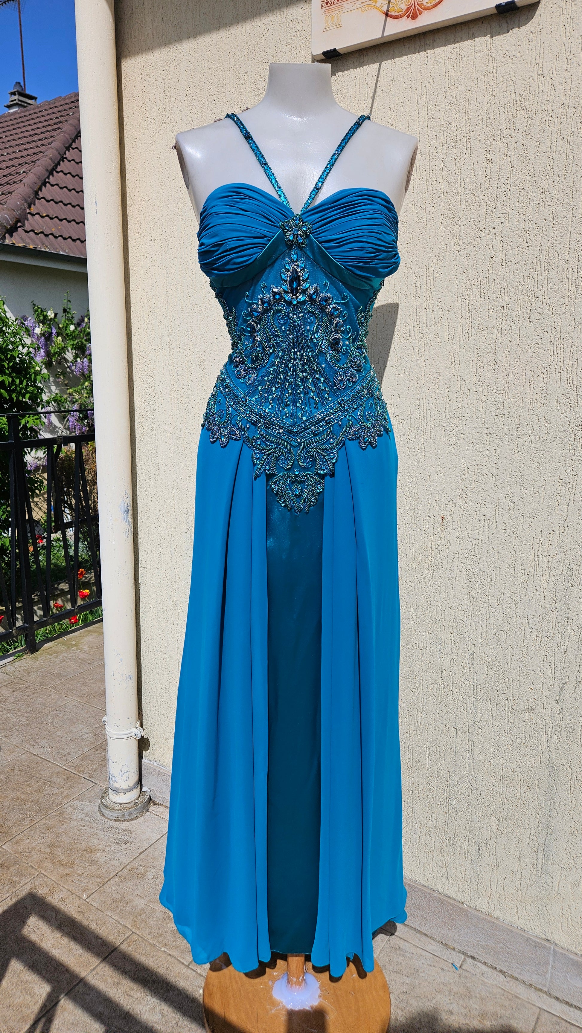 Turquoise blue chiffon evening gown with halter neck, pleated bust, and ornate teal bead & crystal bodice embroidery. Elegant mermaid style formal dress.