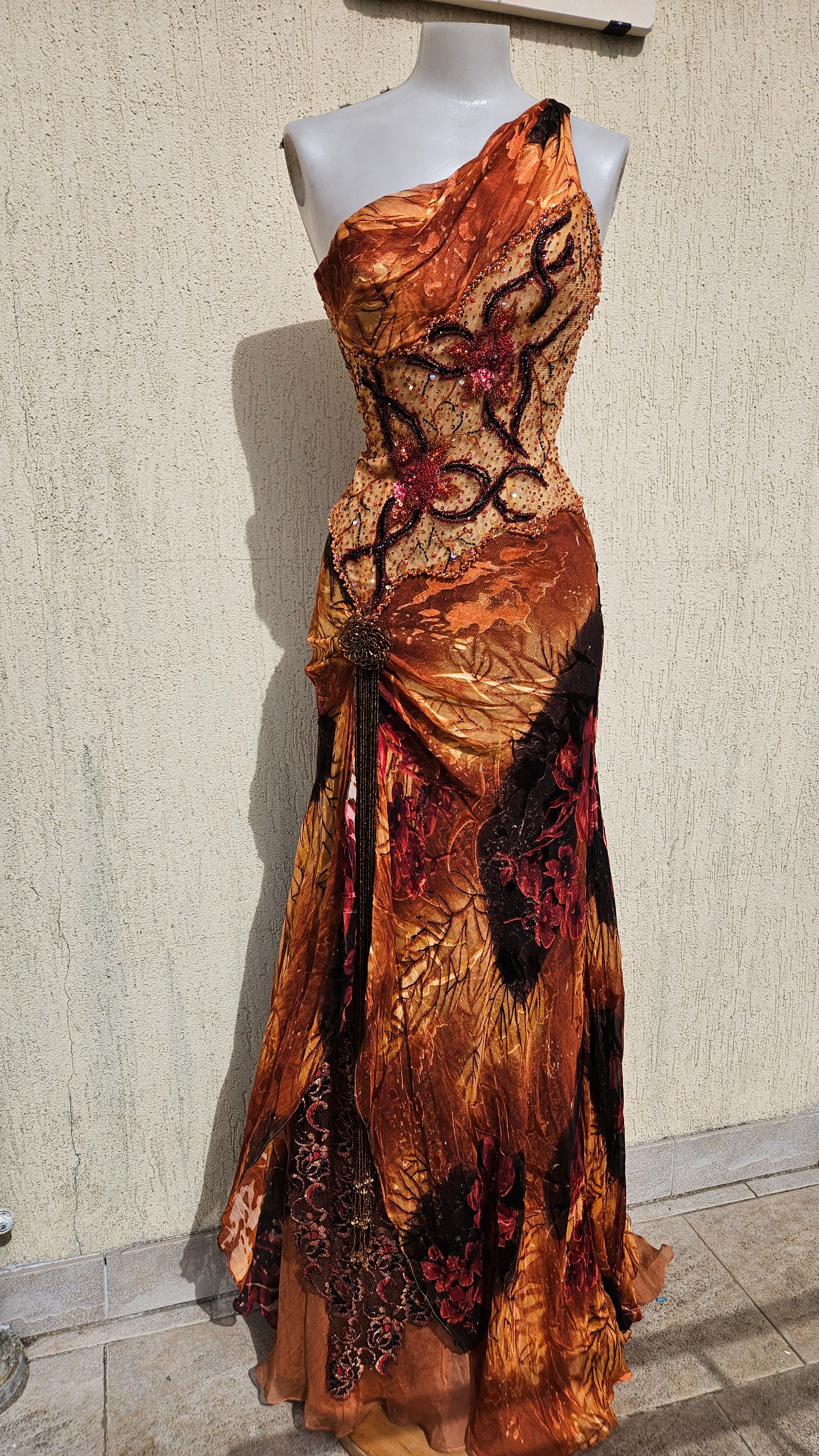 Vintage Y2K orange one-shoulder maxi dress on a mannequin. Intricate beaded bodice, layered mixed-print skirt, and side tassel. Art-to-wear evening gown.