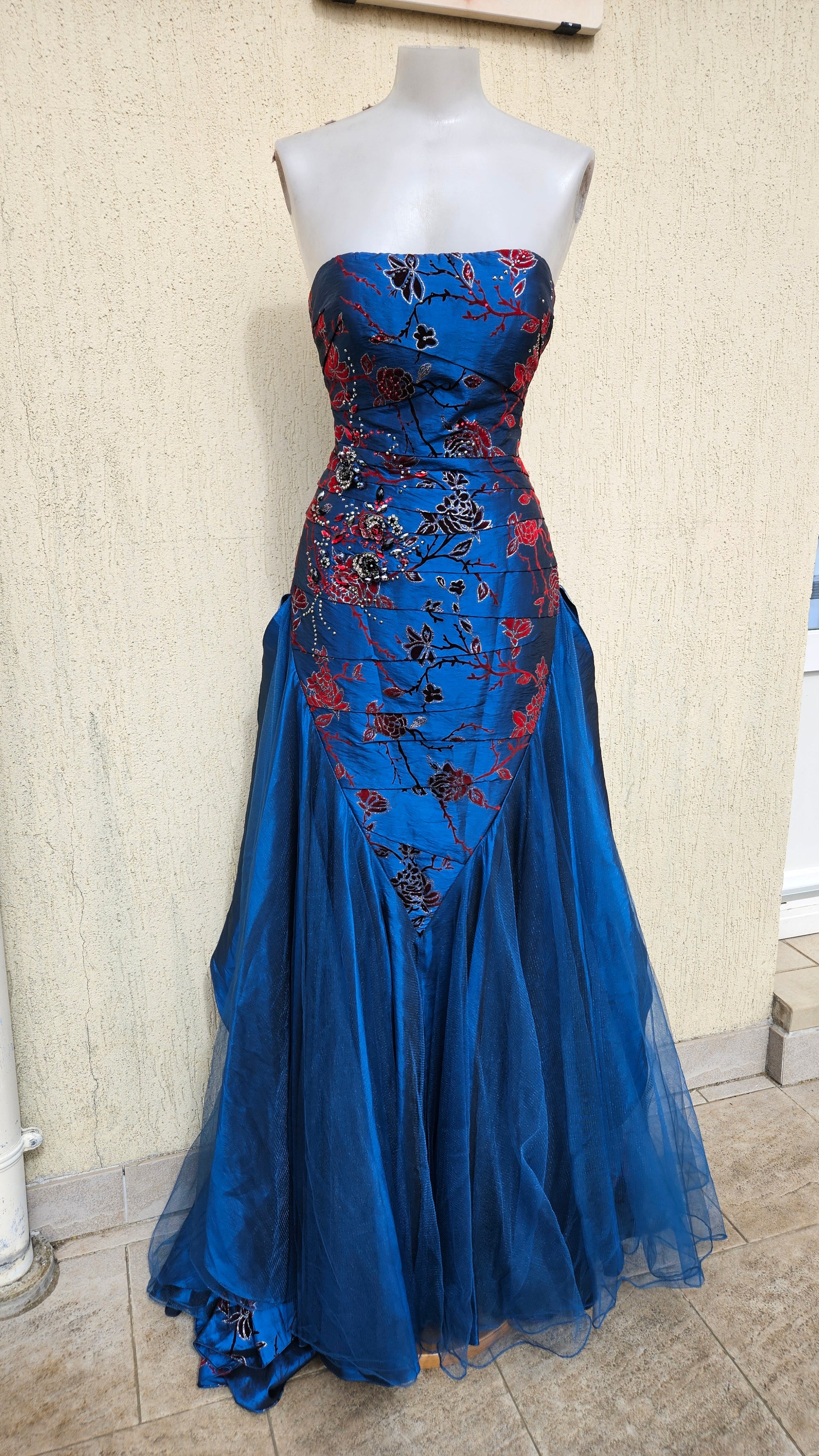 Strapless royal blue evening gown with red and black floral embroidery, sequined bodice, and a voluminous tulle mermaid skirt for formal galas or prom.