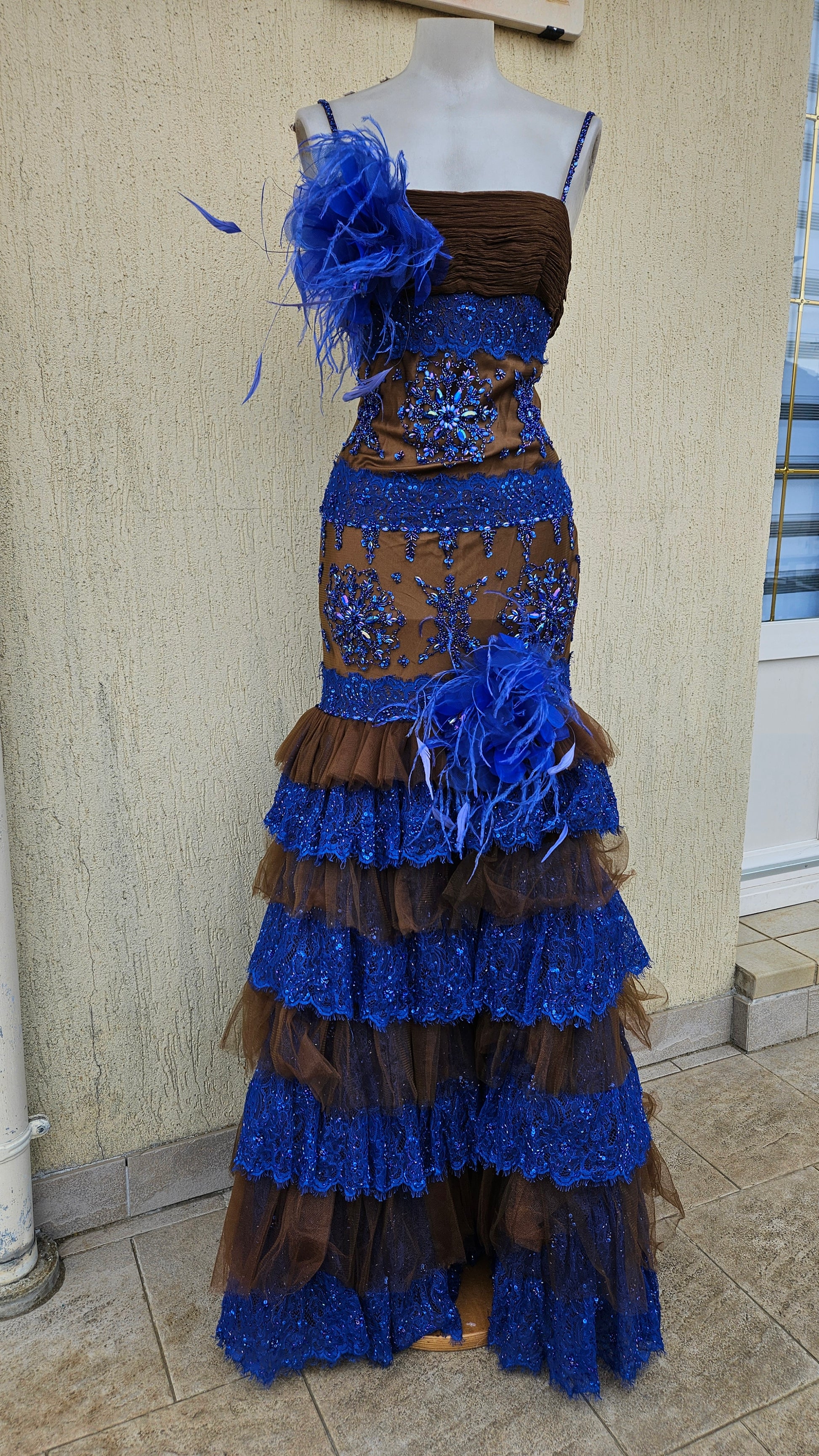 Unique blue and brown mermaid evening gown with detailed sequin embroidery, feather accents, and tiered tulle/lace skirt.