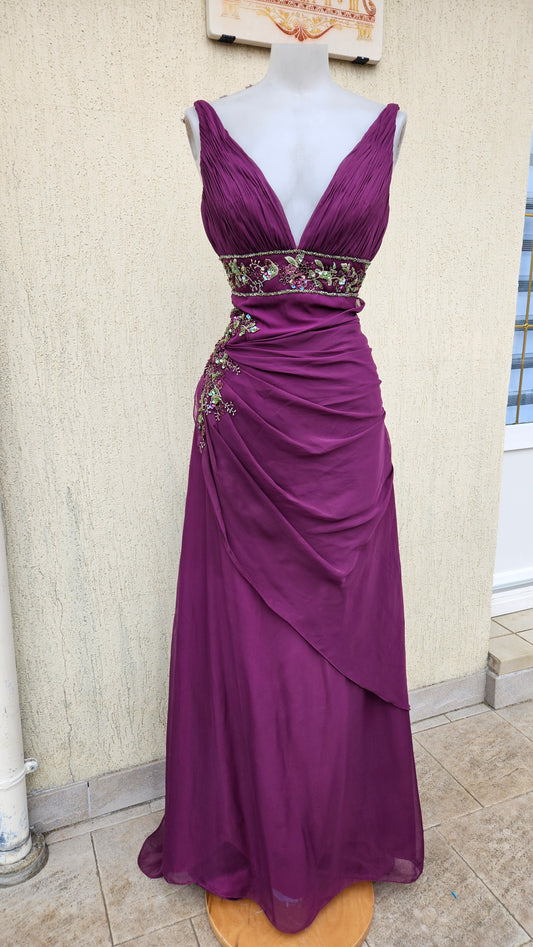 Deep plum pleated chiffon evening gown with V-neck, floral beaded empire waist, and asymmetrical side drape on a mannequin.
