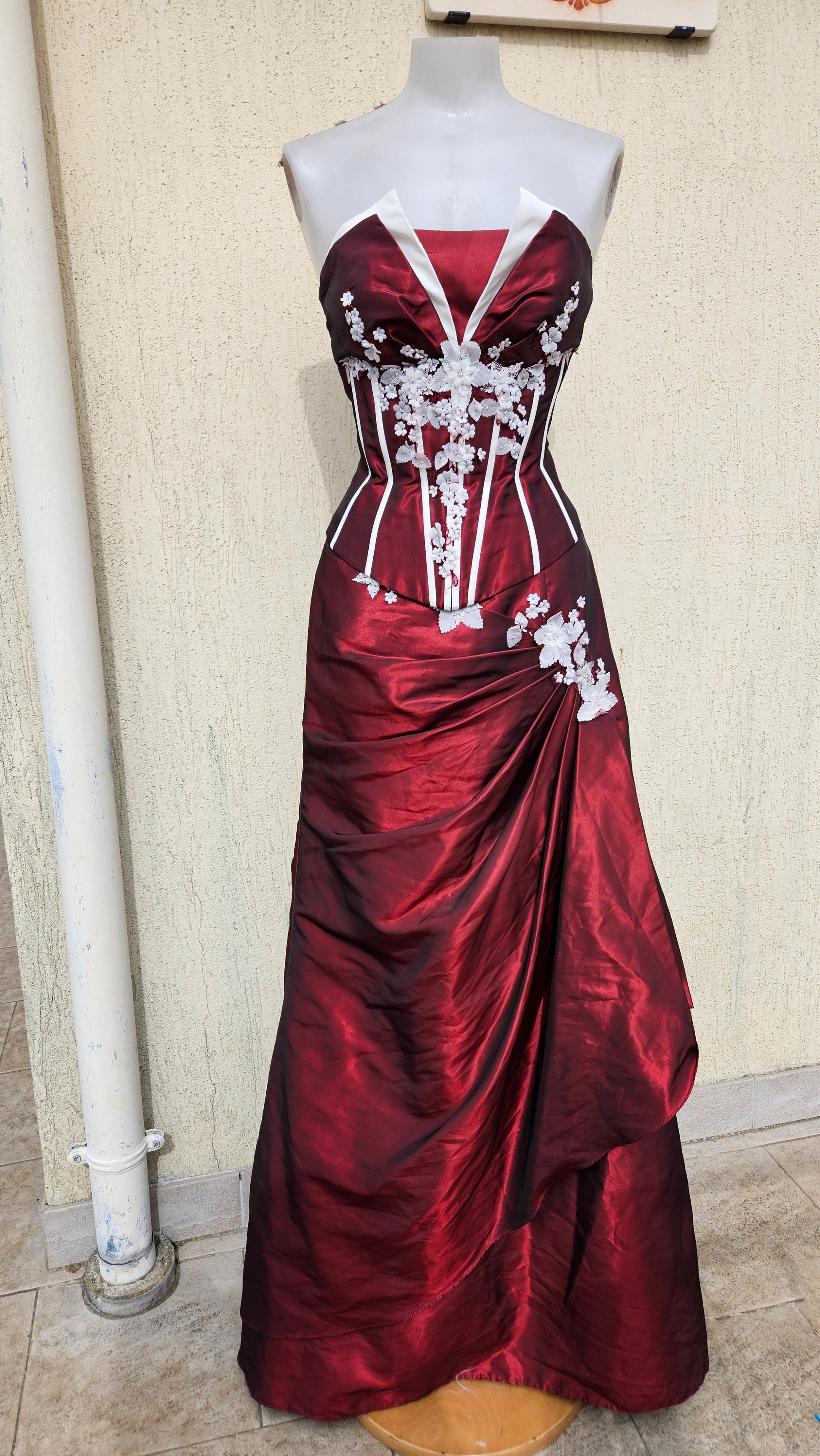 Striking strapless crimson and white corset gown with floral embroidery on a mannequin.