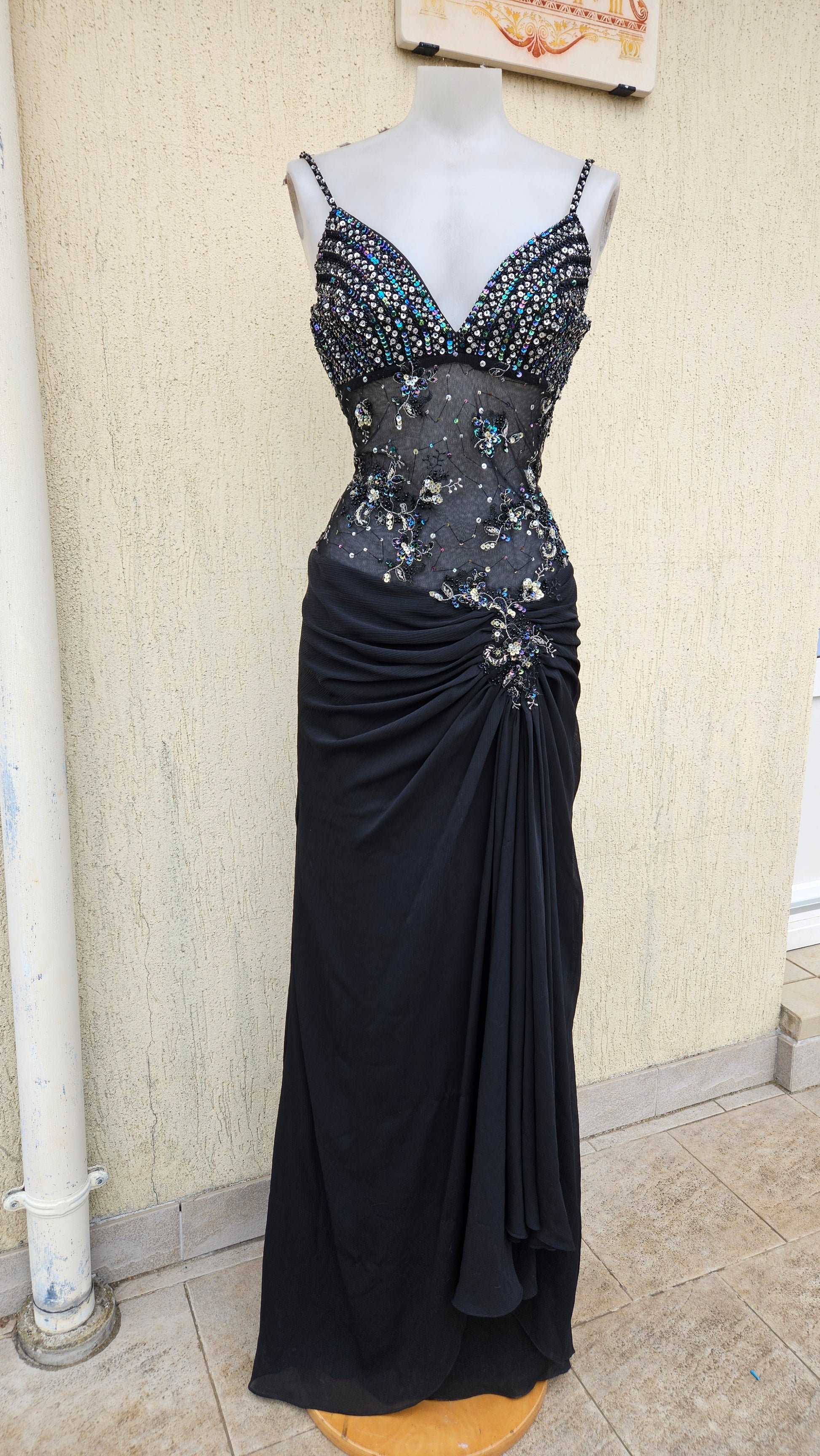 Vintage Y2K black maxi gown on a mannequin with a sequined bodice, sheer beaded midriff, and elegant side-draped skirt. Perfect for formal events or prom.