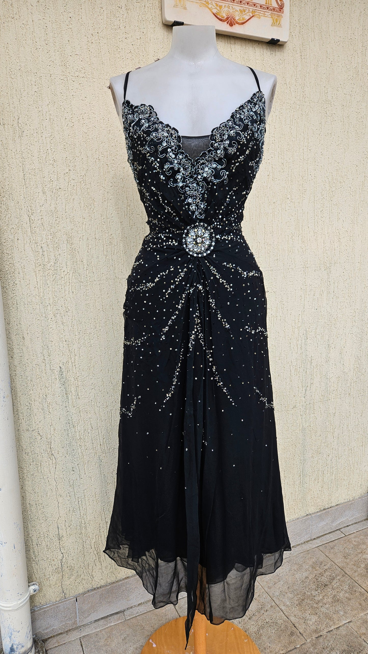 Glamorous vintage Y2K black midi dress on a mannequin, featuring heavy silver sequin and bead embellishments, a detailed crystal broach waist, and sheer mesh hem.