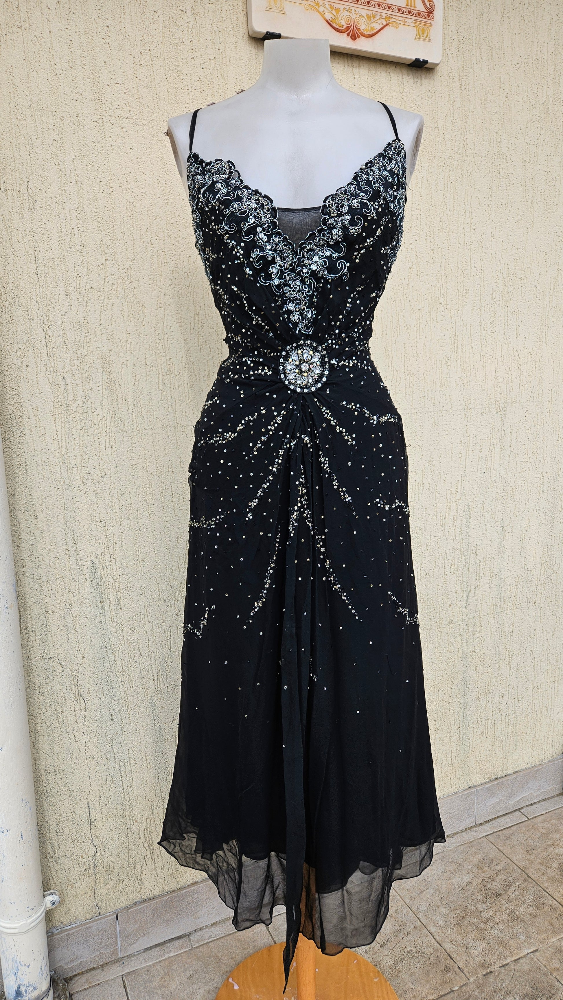 Glamorous vintage Y2K black midi dress on a mannequin, featuring heavy silver sequin and bead embellishments, a detailed crystal broach waist, and sheer mesh hem.