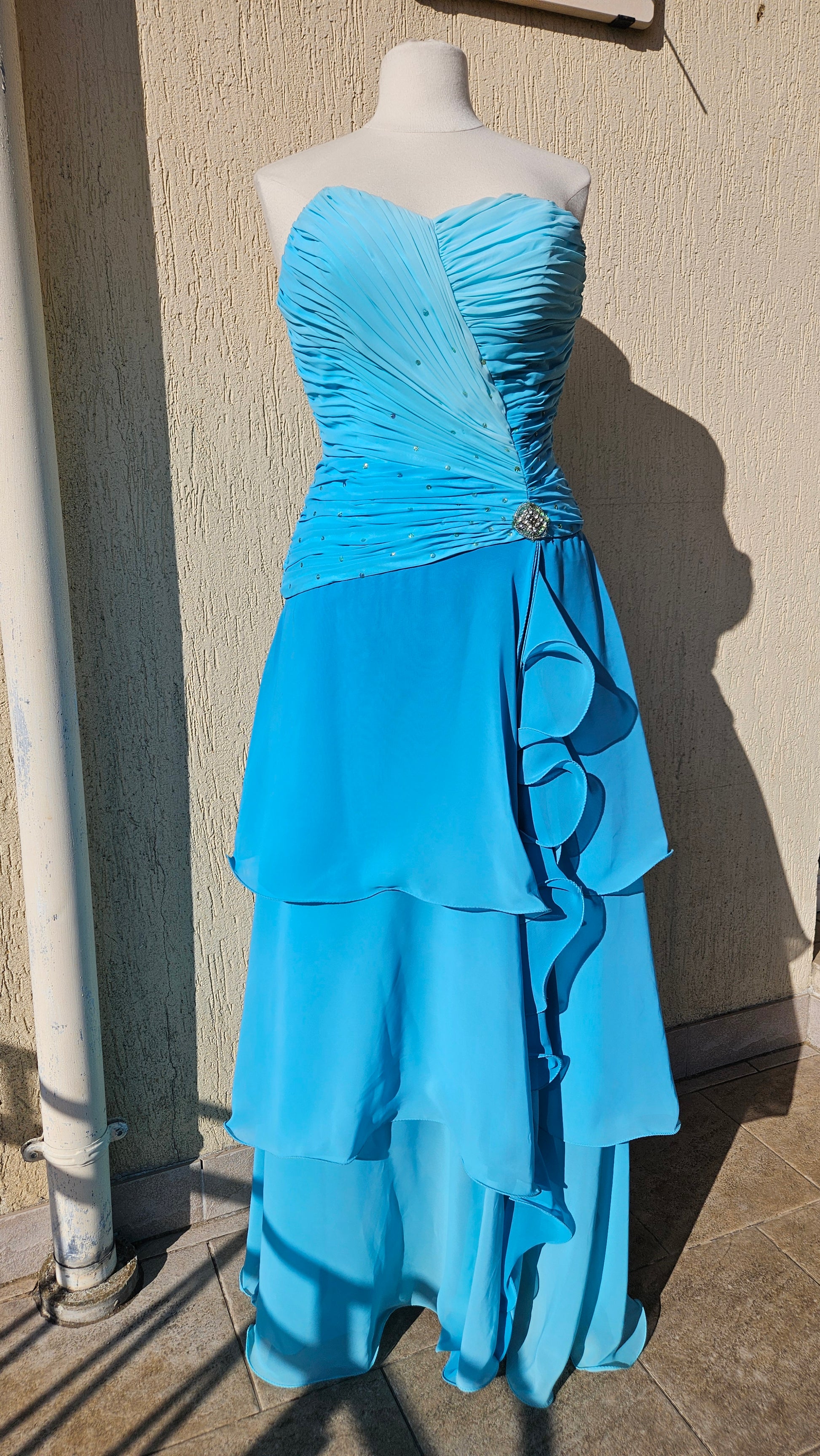Robe de soirée bustier vintage Y2K bleu turquoise. Corsage drapé orné de strass avec une broche bijou, et jupe longue en mousseline à volants étagés. Le look ultime de reine du bal des années 2000.